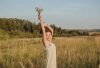 A joyful woman in a white dress holds wildflowers in a sunny field, embracing the serene summer outdoors.