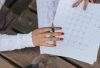 From above crop anonymous female in white blouse sitting at wooden table with pen and making list of plans for month